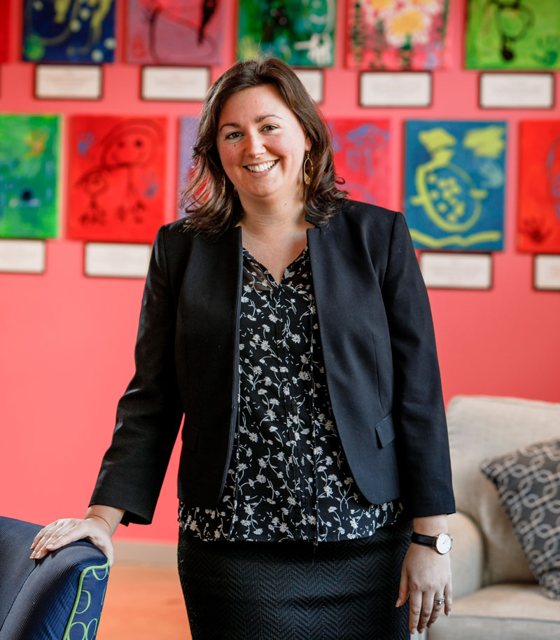 honorary degree speaker Aly Richard poses in a blazer in front of a red wall of children's artwork