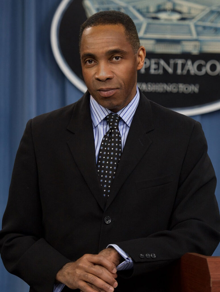 headshot of JJ Green wearing a black suit standing in front of a Pentagon sign